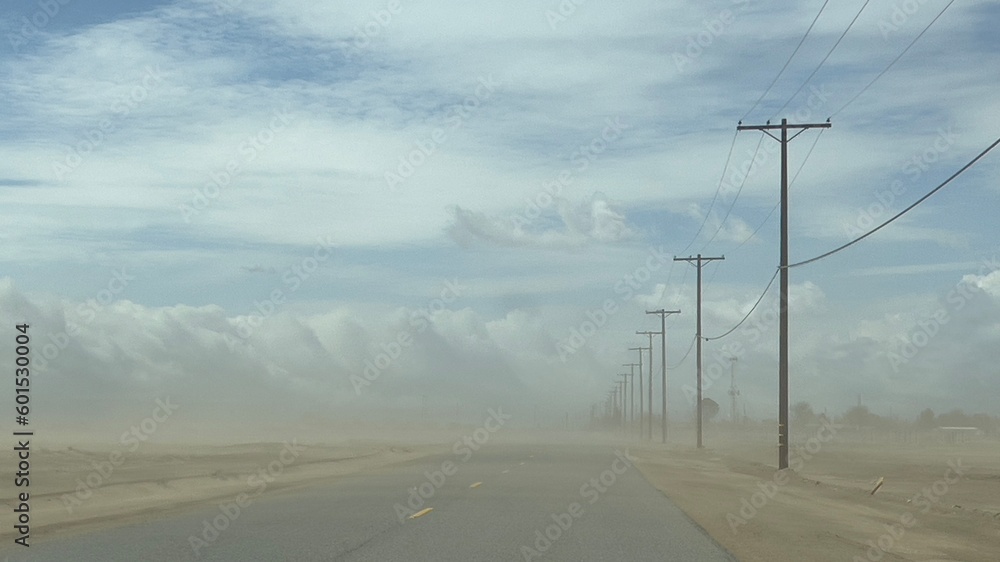 Wide view dust storm on desert highway in southern California, with telegraph poles at side of the road, fading into distance