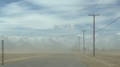 Wide view dust storm on desert highway in southern California, with telegraph poles at side of the road, fading into distance