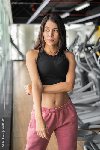 Slim female model with straight hair wears a sports top and pants, young latin woman, gym interior, healthy lifestyle and person portrait