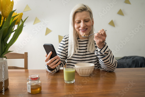 Blonde caucasian woman eating corn flakes and using her smartphone