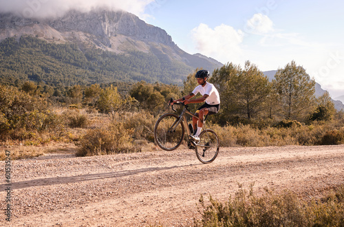 Man cyclist on gravel bicycle riding wheelie on a rear wheel.Cyclist practicing on gravel road.Gravel biking. Extreme sports and activity concept.Spain