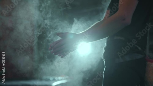 A millennial male rock climber claps his hands with magnesia against a bright lantern during a night workout. Magnesia dust flies out of the hands after the cotton. High quality 4k footage