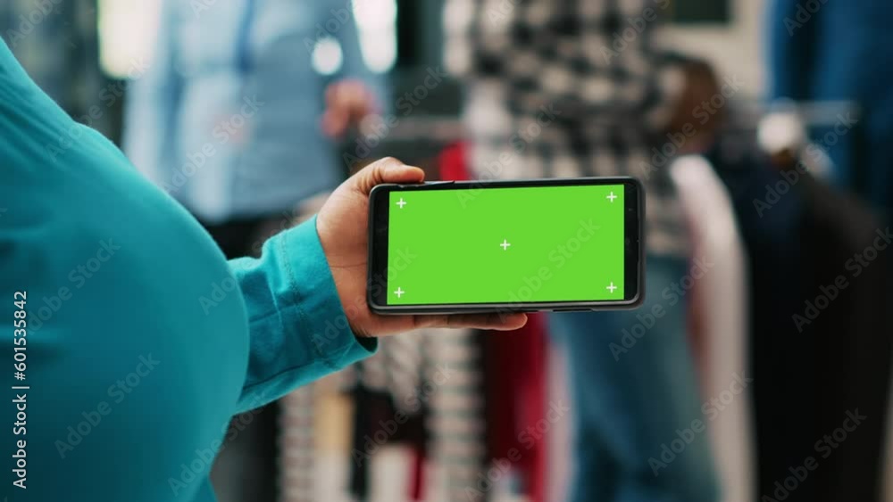 African american client looking at phone with greenscreen template, analyzing isolated display in modern boutique. Stylish woman shopping for casual wear in clothing store. Fashion concept African american client looking at phone with greenscreen template, analyzing isolated display in modern boutique. Stylish woman shopping for casual wear in clothing store. Fashion concept