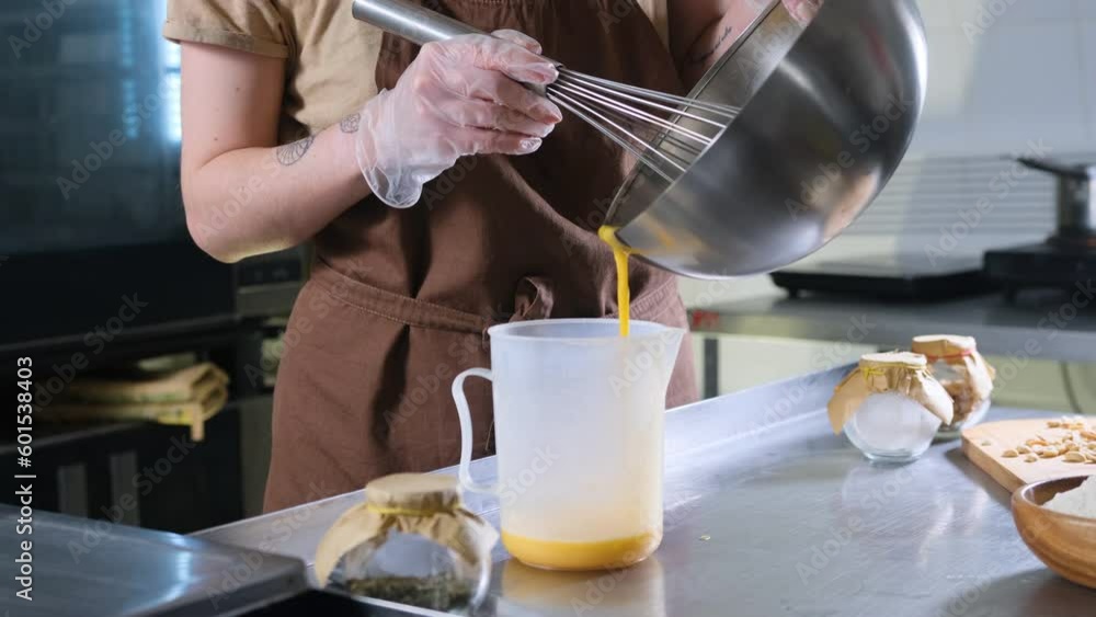Pouring liquid from beaten eggs into a large bowl Female chefs prepare a culinary product or dough Pouring liquid from beaten eggs into a large bowl Female chefs prepare a culinary product or dough