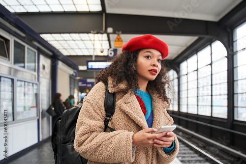 Curly brunette girl standing at the tram station and holding smartphone