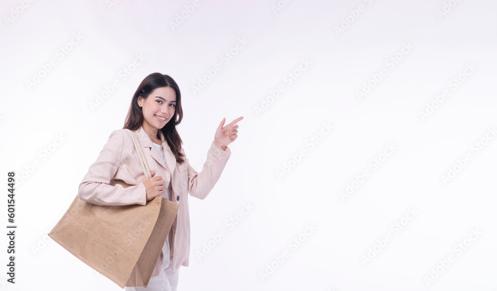 Excited cheerful asian woman wear suit carry eco tote handbag pointing finger choose empty standing on isolated white background. Shopper girl use finger point to camera shopping online advertisement. Excited cheerful asian woman wear suit carry eco tote handbag pointing finger choose empty standing on isolated white background. Shopper girl use finger point to camera shopping online advertisement.