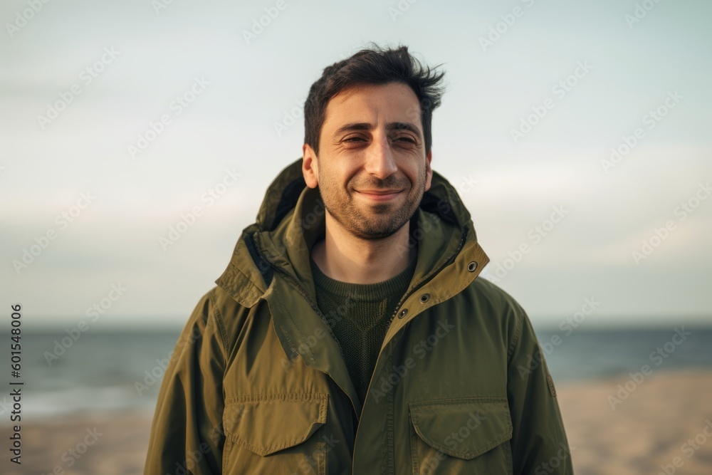 Portrait of a handsome young man in a green jacket standing on the beach