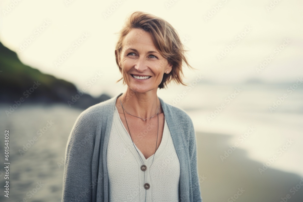 Portrait of smiling mature woman standing on beach at sunrise in summer Portrait of smiling mature woman standing on beach at sunrise in summer