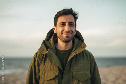 Portrait of a handsome young man in a green jacket standing on the beach