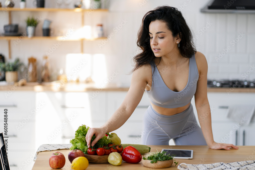 Portrait of beautiful fit woman preparing fresh salt with fruits and vegetables standing on modern kitchen. Vegetarian diet, healthy lifestyle concept 