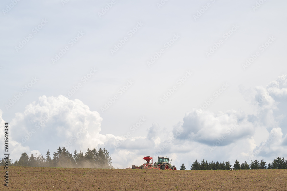 Fototapeta premium Sämaschine bei der Aussaat, vor Quellwolken
