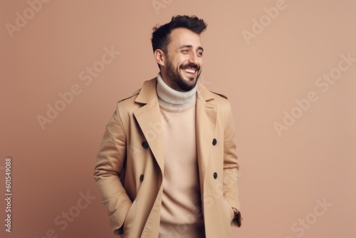 happy young man in beige coat smiling at camera isolated on beige