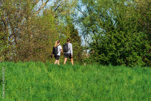 A couple of people walking in a lush green field in the open air, two girls with backpacks on a walk in an eco-city, spring vegetation on a sunny day, authentic sustainability, youth hiking © Александр Бочкала