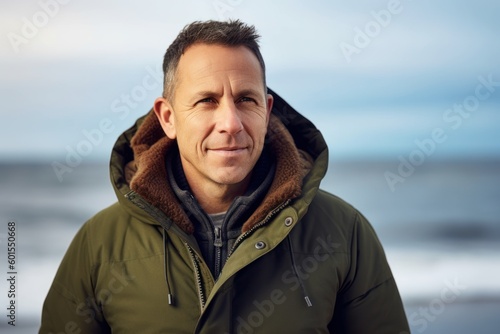 Portrait of handsome man in winter jacket standing on beach, looking at camera