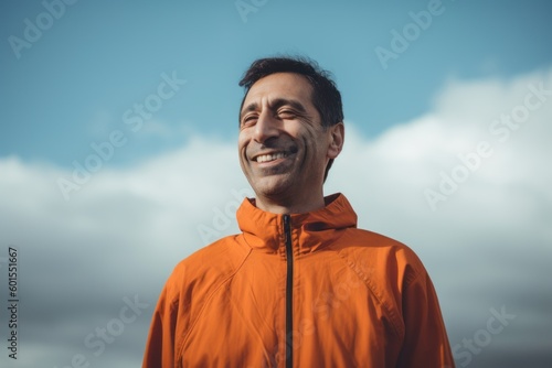 Portrait of a smiling man in an orange jacket against the blue sky.