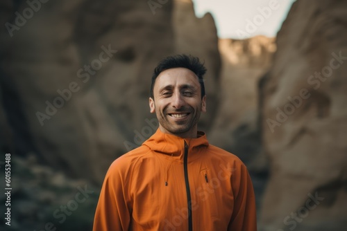 Handsome young man in an orange jacket standing in the mountains