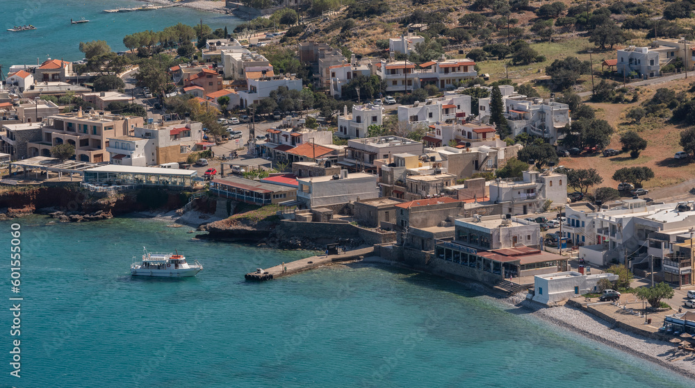 Plaka, Elounda, Crete, Greece. 2023. Overview of the  resort of Plaka and a small ferry boat inbound from the Fortress island of Spinalonga a former Leper Colony.