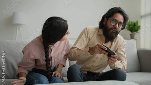 Indian woman wife distract husband from playing virtual game focused Arabian muslim man addicted play tv console videogame use joystick male funny gamer ignoring overuse gaming ignorance family crisis