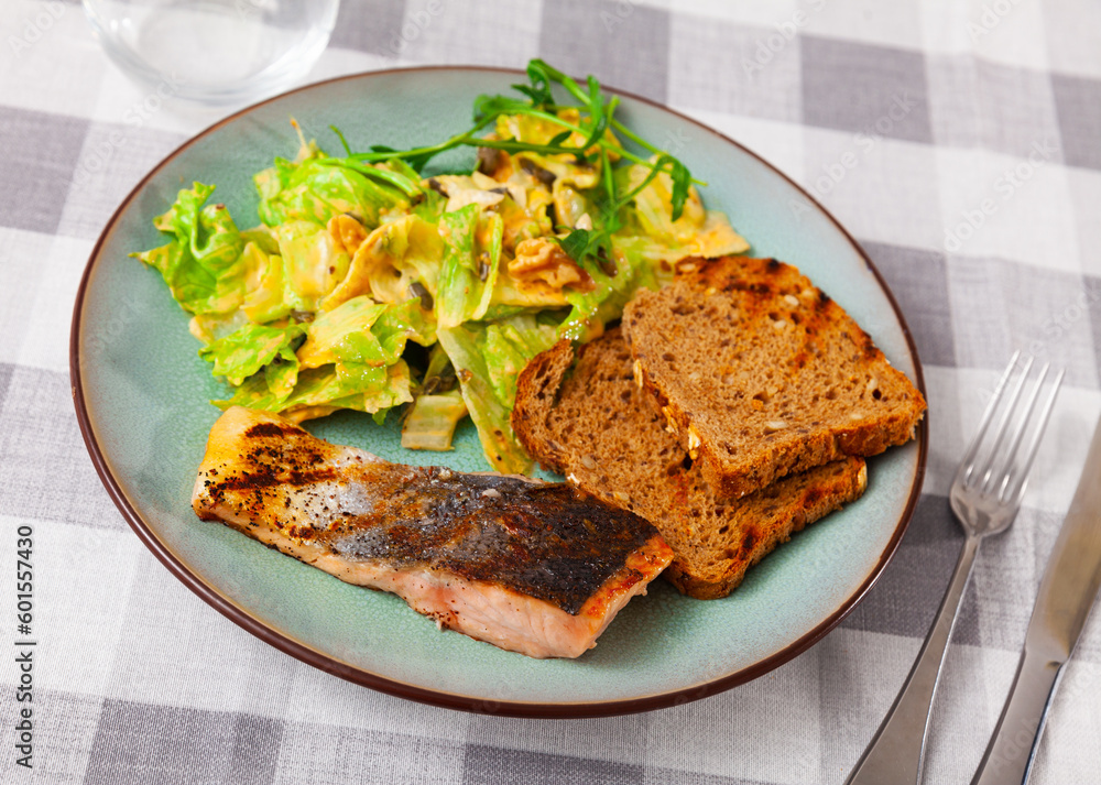 Appetizing baked salmon steak with spices with delicious vegetable salad, served with bread