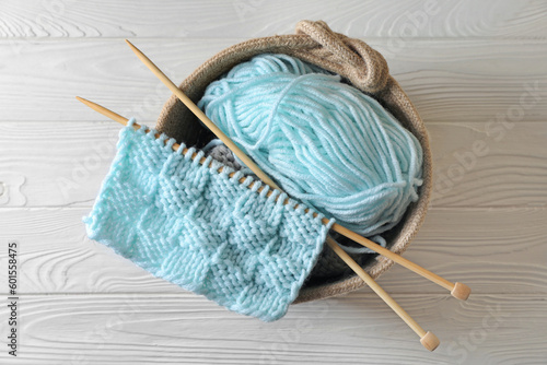 Soft turquoise yarn, knitting and needles on white wooden table, top view