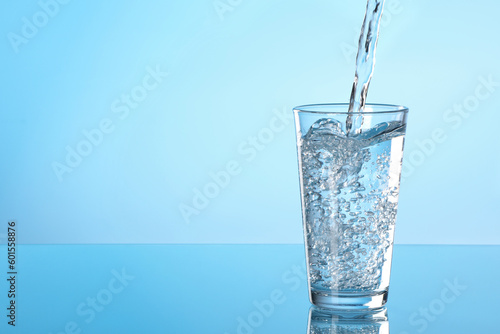Pouring water into glass on light blue background. Space for text