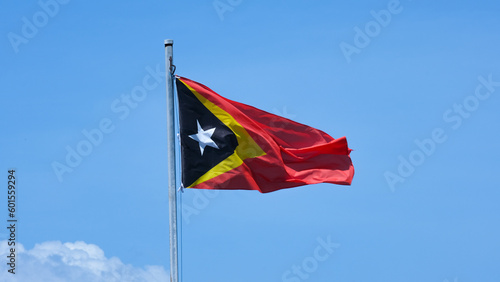 Timor-Leste national flag on flagpole flying in the wind against a blue sky in Southeast Asia country