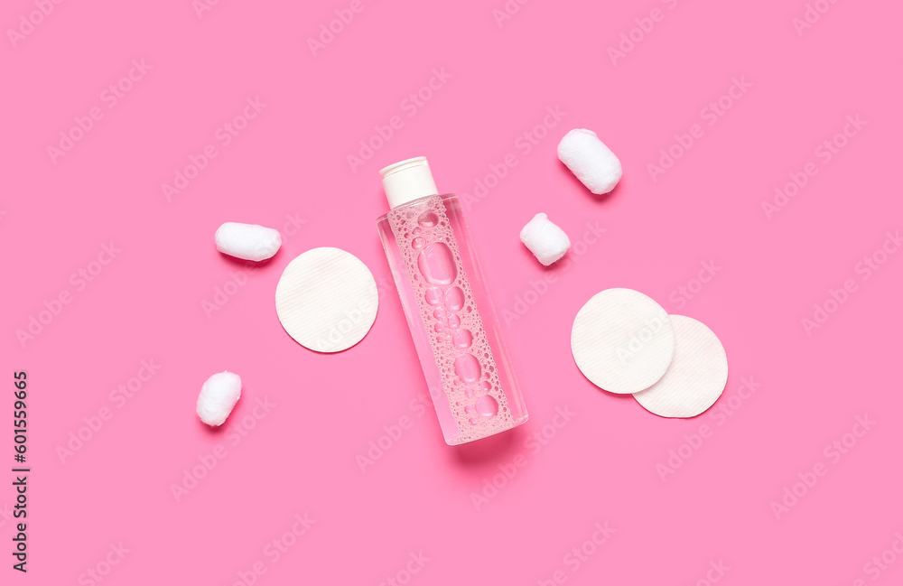 Bottle of micellar water with cotton balls and pads on pink background Bottle of micellar water with cotton balls and pads on pink background
