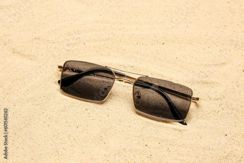 Stylish sunglasses on sand, closeup