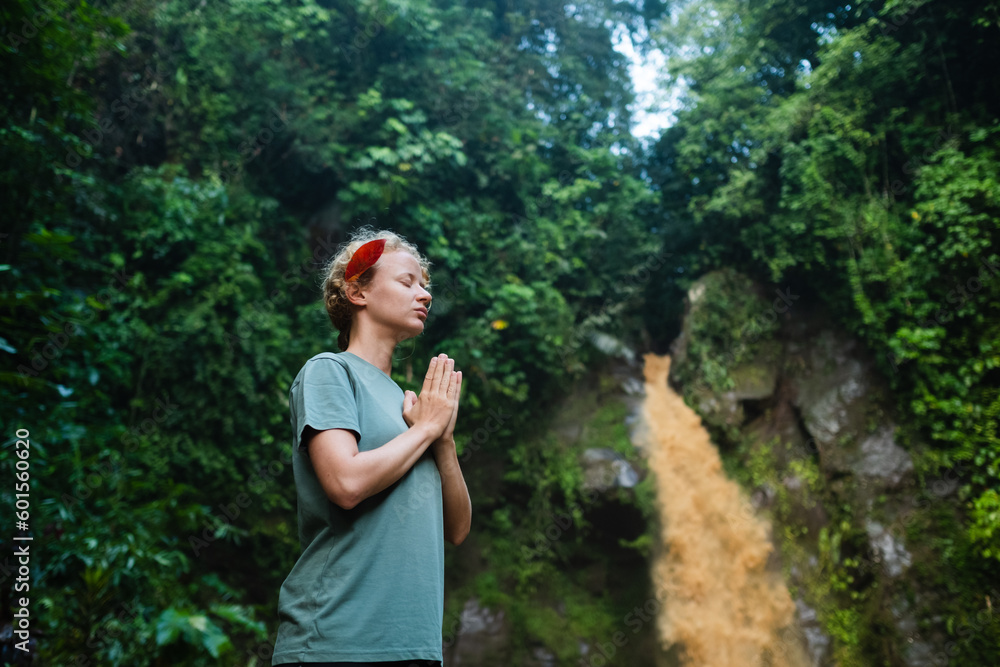 The girl is meditating, her hands are folded in namaste, in the jungle against the backdrop of a waterfall. The girl is meditating, her hands are folded in namaste, in the jungle against the backdrop of a waterfall.