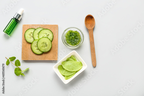 Bowls with cotton under-eye patches, cucumber slices, mint and dropper bottle on light background