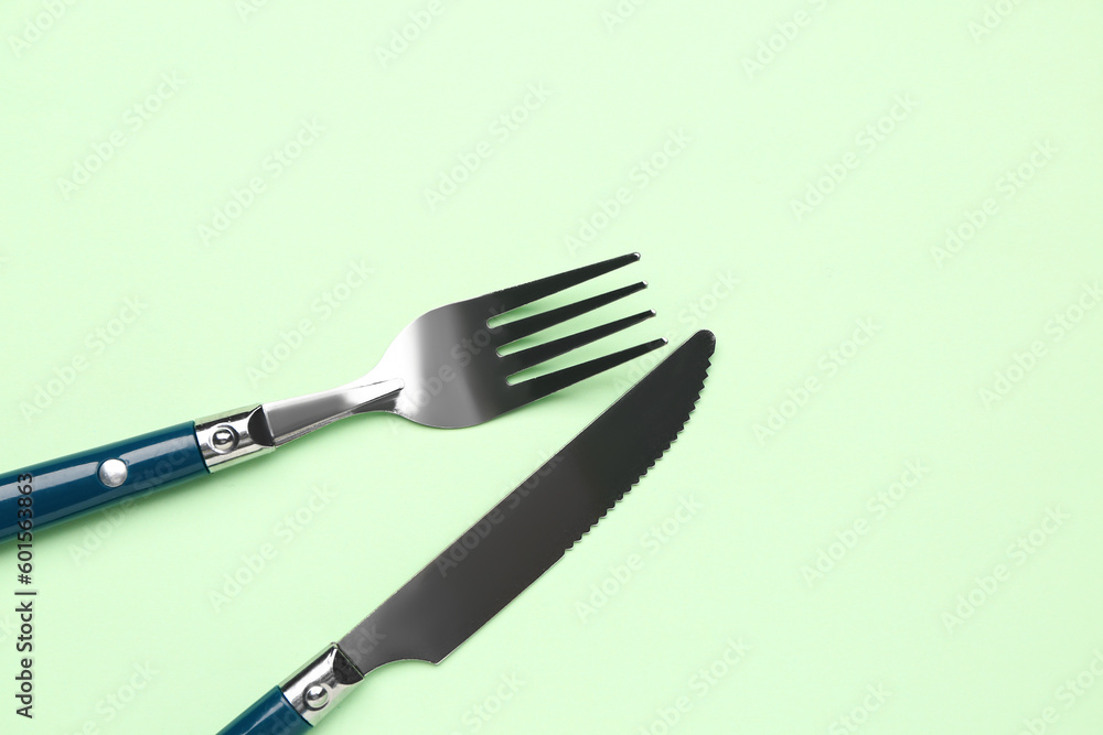 Stainless steel fork and knife with plastic handle on green background Stainless steel fork and knife with plastic handle on green background