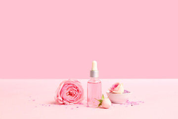 Bottle of cosmetic oil with rose extract and flowers on pink background