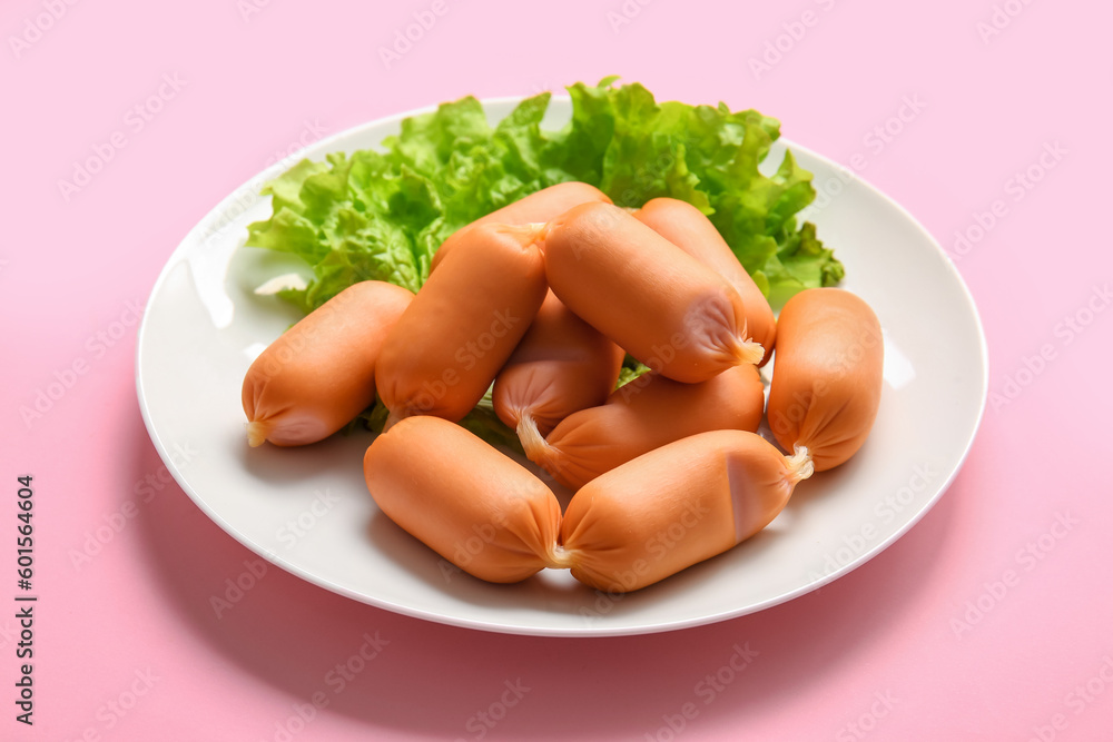 Plate of tasty boiled sausages with lettuce on pink background Plate of tasty boiled sausages with lettuce on pink background