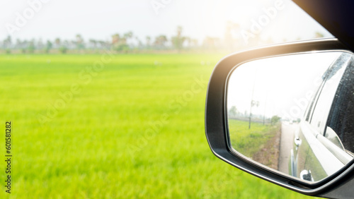 View of beside mirror wing of car can view cars behind in the distance on asphalt road. background image is a yellow-green rice field in the morning.