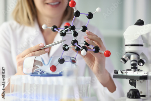 Woman in white lab coat demonstrates model of molecule