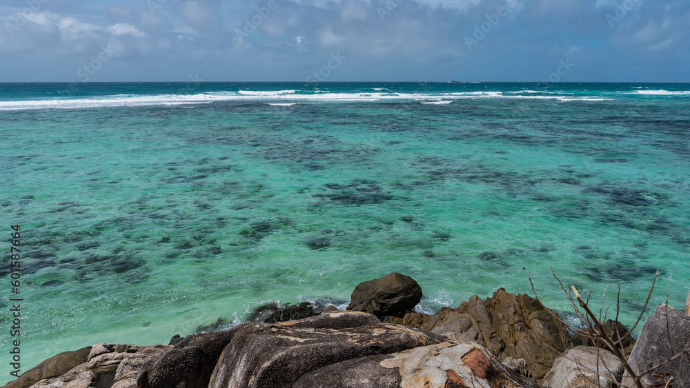 The boundless turquoise ocean stretches to the horizon. Clear water and foam waves over the reef. Granite rocks in the foreground. Clouds in the sky. Seychelles. Moyenne Island. The boundless turquoise ocean stretches to the horizon. Clear water and foam waves over the reef. Granite rocks in the foreground. Clouds in the sky. Seychelles. Moyenne Island.