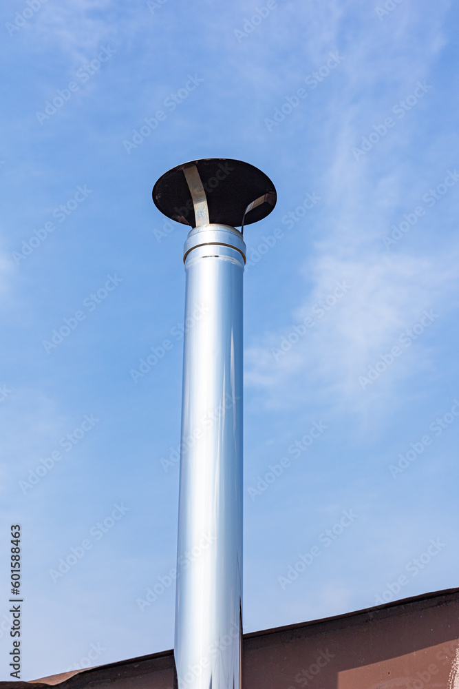 Exterior metal chimney pipe on top of a roof, clean new shiny chimney pipe on blue-sky background. Air vent system on the top of the house. Modern round steel chimney on rooftop