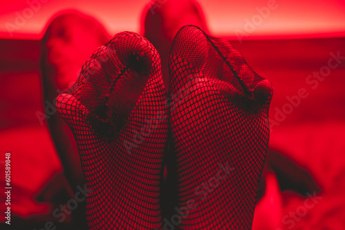 Details of sexy legs and feet in fishnet stockings in bed under seductive and intimate red light