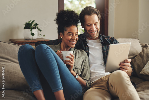 Relax, home and interracial couple on a couch, tablet and happiness with social media and connection. Partners, man and woman on a sofa, technology and loving with a smile, romance and online reading