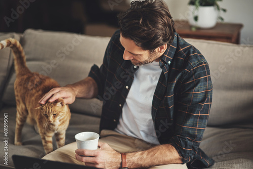 Love, coffee and man with his cat on a sofa to relax and bond together in his modern home. Rest, animal and male person rubbing his kitten pet with care while drinking a latte in living room at home.