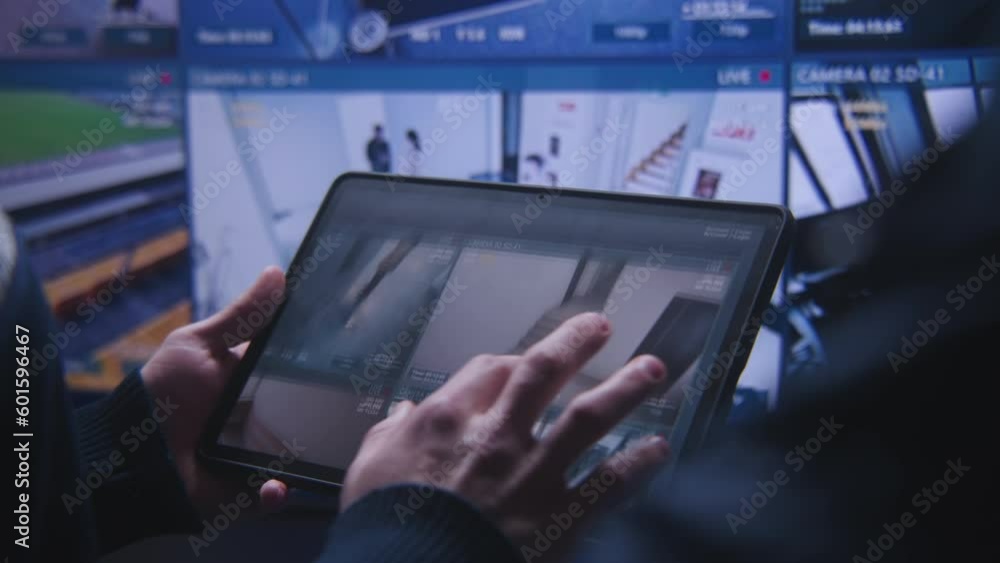 Close up shot of operator zooming and monitoring CCTV cameras using tablet in police surveillance center. Big screen on the wall showing security cameras with AI face scanning footage. Social safety. Close up shot of operator zooming and monitoring CCTV cameras using tablet in police surveillance center. Big screen on the wall showing security cameras with AI face scanning footage. Social safety.