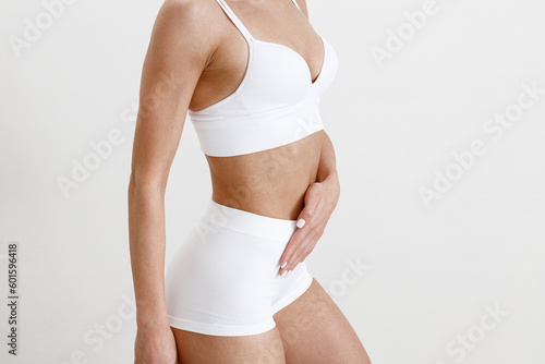 Slim and beautiful female body wearing white lingerie showing ideal curves on studio background