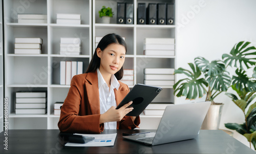  Beautiful Asian business woman typing laptop and tablet Placed at the table at the office © laddawan