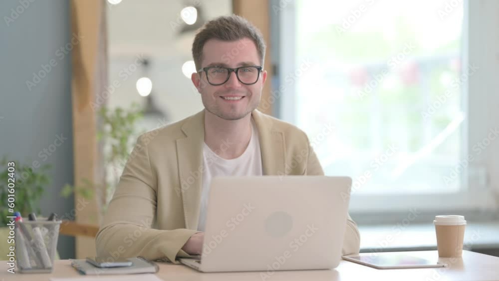 Young Businessman Smiling at Camera while Working on Laptop Young Businessman Smiling at Camera while Working on Laptop