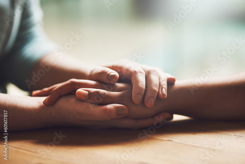 Foto Love, empathy and support with people holding hands in comfort, care or understanding on a wooden table of a home