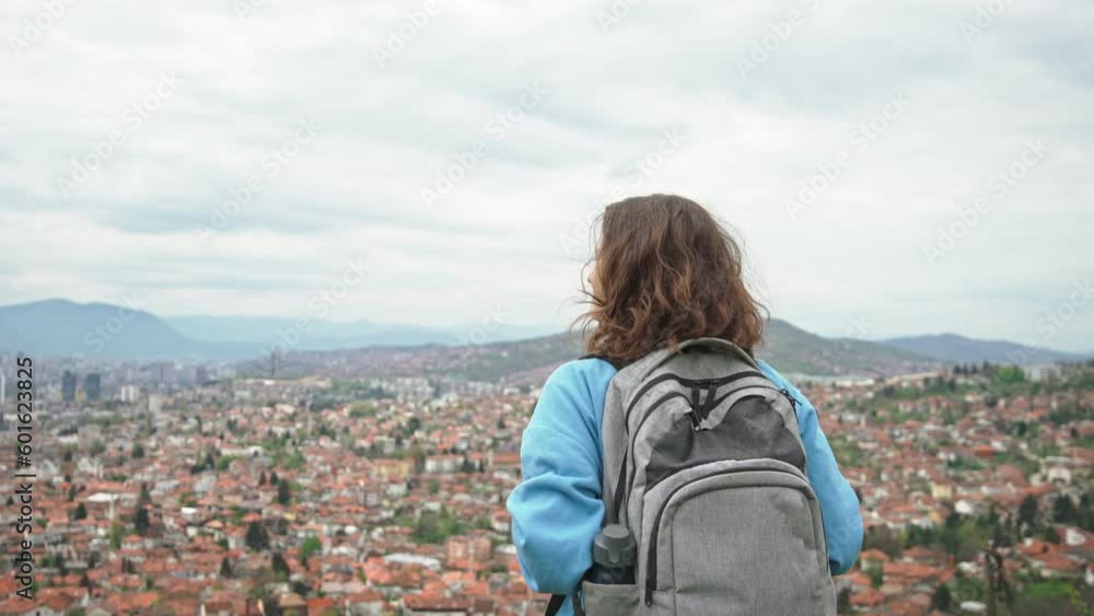 A young Caucasian woman with a backpack enjoying a beautiful top view of the city of Sarajevo A young Caucasian woman with a backpack enjoying a beautiful top view of the city of Sarajevo