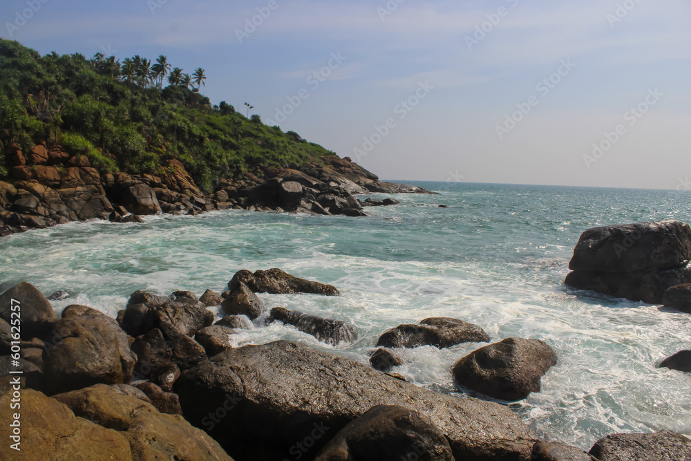 Dark rocks and beautiful palm trees in the sun at Jungle Beach, Unawatuna, Sri Lanka, blue sky with clouds, copy space for text
