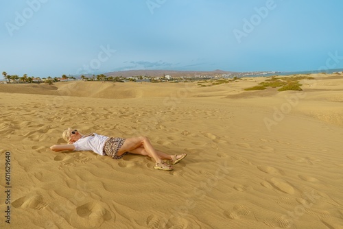 A tourist woman visiting the Maspalomas Dunes of Gran Canaria simply relaxes and sunbathes on the nearby Maspalomas Beach. Maspalomas Dunes of Gran Canaria sunbathing on the nearby Maspalomas Beach.
