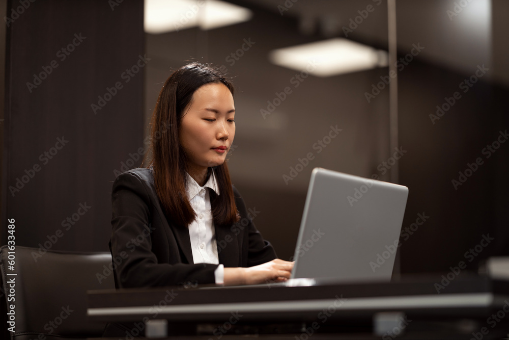 A beautiful Chinese woman is working on a laptop in her office. She is wearing formal clothes. A beautiful Chinese woman is working on a laptop in her office. She is wearing formal clothes.