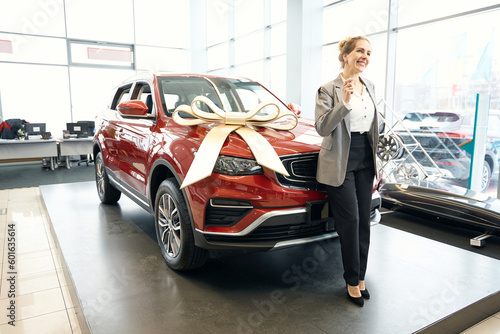Happy lady standing in front of red automobile in cardealership